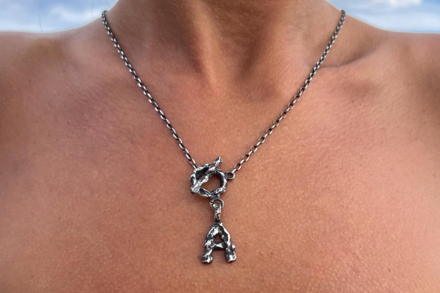 Silver necklace with a unique letter pendant on a person.