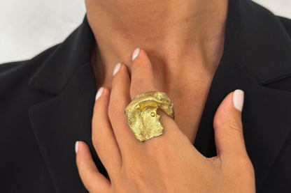 Hand wearing a large gold plated brass freeform ring with a textured design.