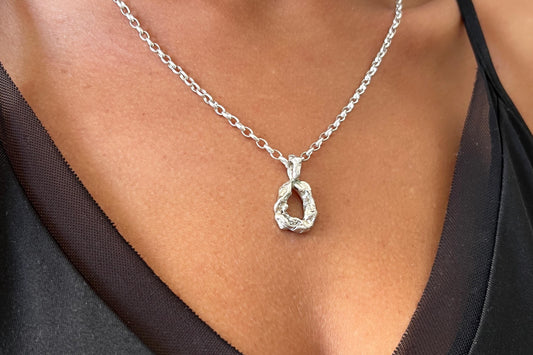 Silver necklace with an initial letter pendant on a person.