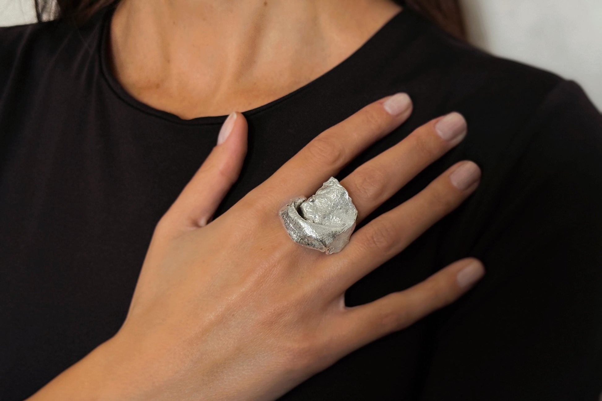 Hand wearing a large, irregular textured sterling silver ring against a black background