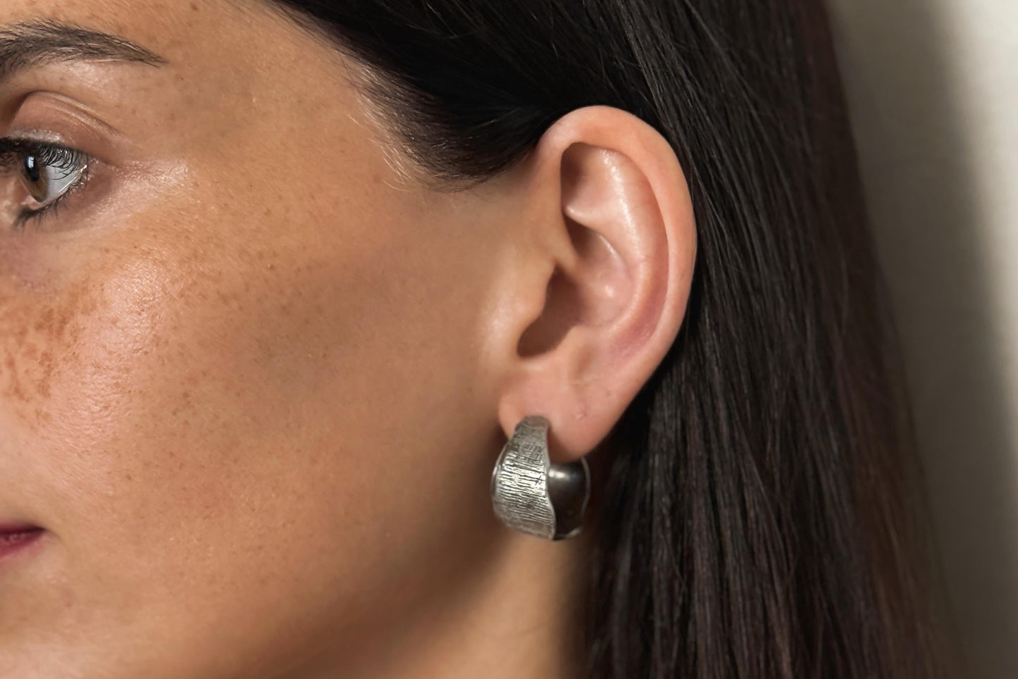 Close-up of a woman's ear wearing a silver hoop earring with a neutral background