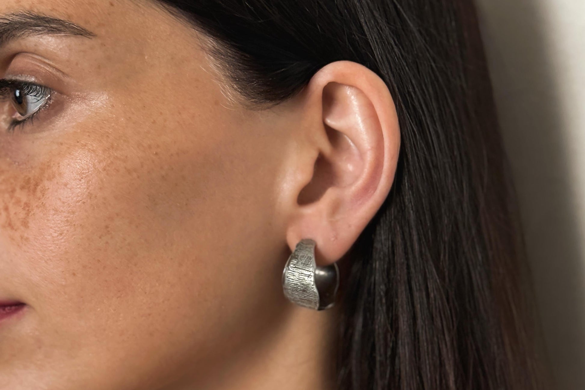 Close-up of a woman's ear wearing a silver hoop earring with a neutral background