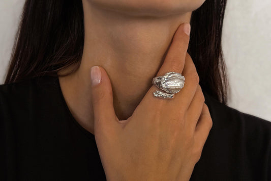 Close-up of a hand wearing a sterling silver ring with a pearl, touching the neck.